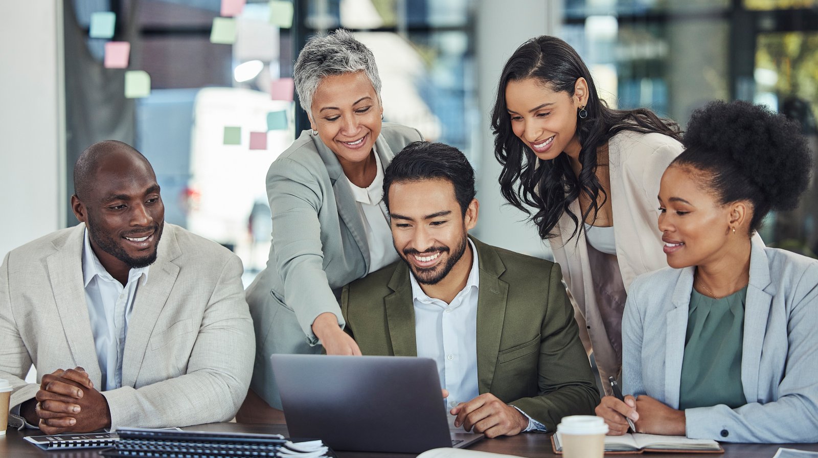 Three colleagues gather around a laptop, smiling and engaged. The atmosphere is collaborative and positive, reflecting teamwork and shared success.